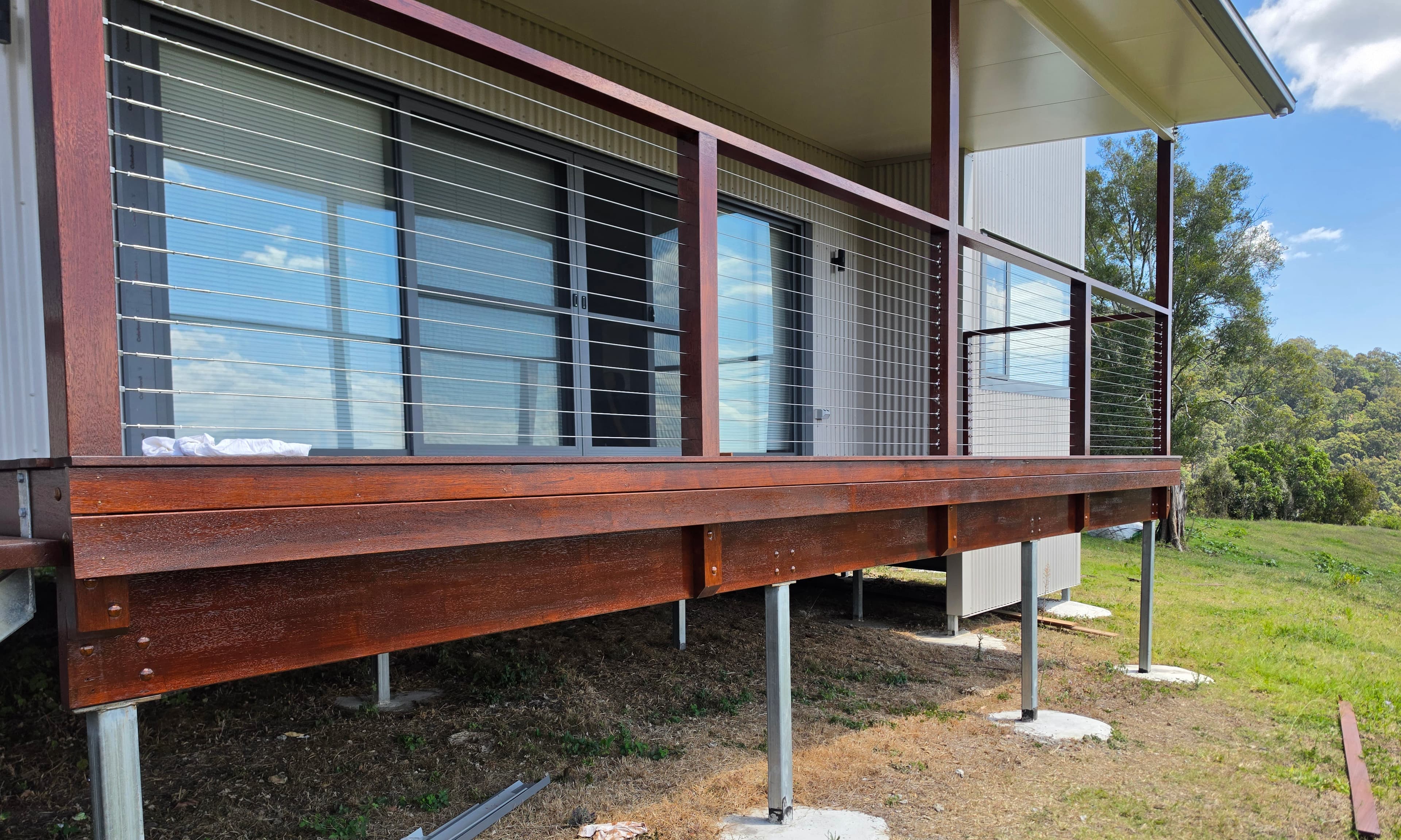 Elevated timber deck with a wire balustrade on steel posts, beside a light-coloured house.